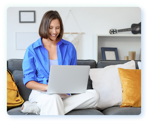A woman sitting on her couch and smiling as she uses her laptop computer.
