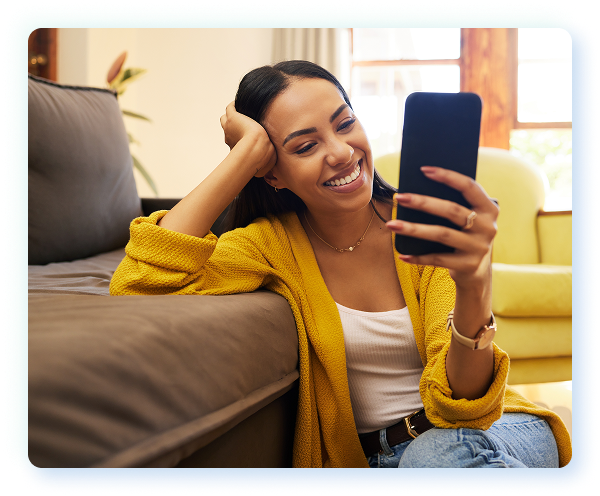 A woman sitting on her couch and smiling as she uses her laptop computer.