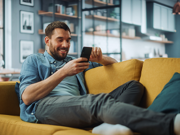A man browsing on his cell phone sitting on a couch in a modern home setting